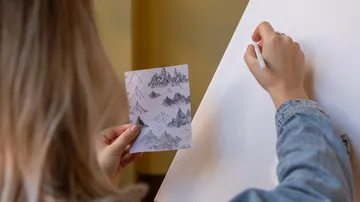 Person skizziert Berge mit Referenzbild.