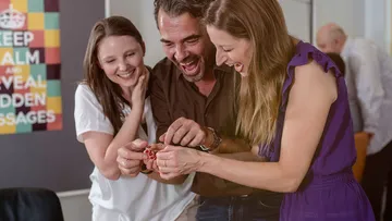Three people excitedly examining object indoors.