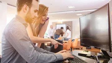 Zwei Personen arbeiten an einem Computertisch.