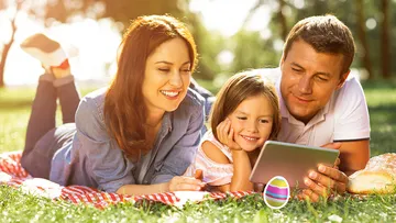Familie schaut Tablet auf Picknickdecke im Freien.