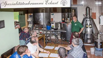 Man lecturing to group in brewery room.
