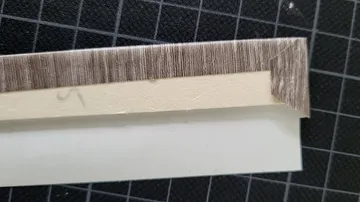 Cardboard corner wrapped in wood-pattern tape.