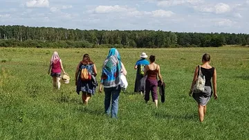 Group walking across grassy field under sky.