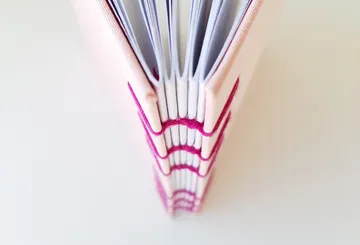 Notizbuch mit rosa sichtbarer Rückenstichnaht.