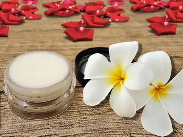 A cream stands next to white flowers on a wooden surface.