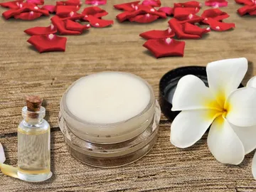 Pflegecreme steht neben einem Fläschchen Öl und einer Blume.