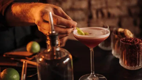 Hand garniert Cocktail mit Limette in dunkler Bar.