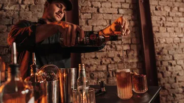 Barkeeper gießt Getränk an rustikaler Bar.