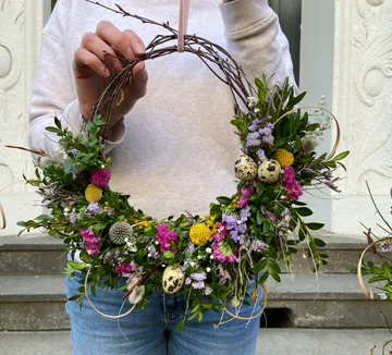 Person holding floral wreath with decorative eggs.