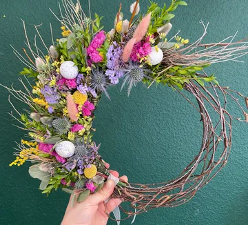 Hand hält dekorativen Blumenkranz vor grüner Wand.