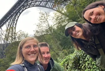Gruppe von Frauen lächelt in der Nähe einer großen Brücke.