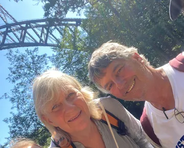 Two people smiling near a steel bridge.