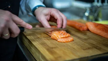 Hände schneiden Lachs auf einem Holzbrett.