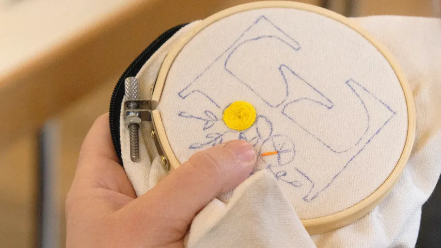 Hand stickt Stoff in einem Holzrahmen.