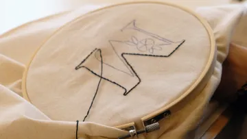 Embroidery showing letter 'M' on fabric.