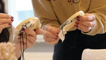 Hände sticken auf Stickrahmen drinnen.