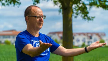 Man practicing tai chi outdoors, green field.