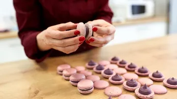 Hands assembling pink macarons in kitchen.