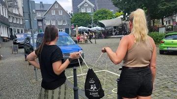 Zwei Frauen stehen mit Tasche auf einem Marktplatz.