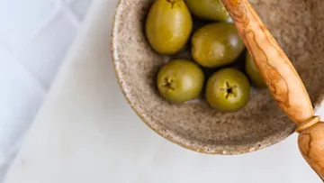 Green olives in a brown bowl with a pestle.