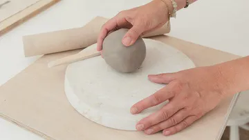 Hands shaping clay on a table.