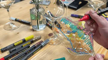 Person decorating wine glass with colorful markers.