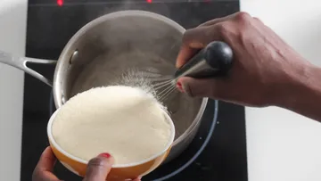 Person whisking semolina into boiling pot.