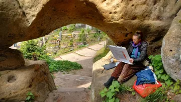 Person drawing under rock arch in garden.