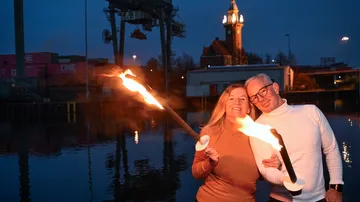 Zwei Personen halten Fackeln am Wasser.