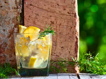 Ein Glas mit Zitronen und Eis steht auf Holz.