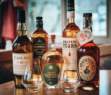Bottles of various whiskeys on wooden table.