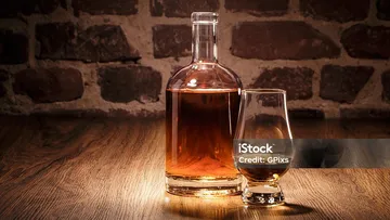 Whiskey bottle and glass on wooden table.