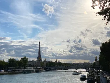 The Eiffel Tower is reflected in the river, surrounded by clouds.