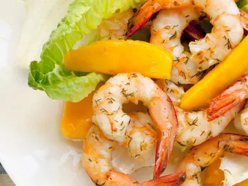 Cooked prawns with salad and mango strips on plate.