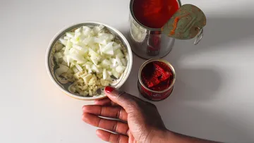Geschnittene Zwiebeln, Knoblauch, offene Tomatendosen auf Tisch.