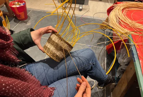 Person weaving basket in craft workshop.