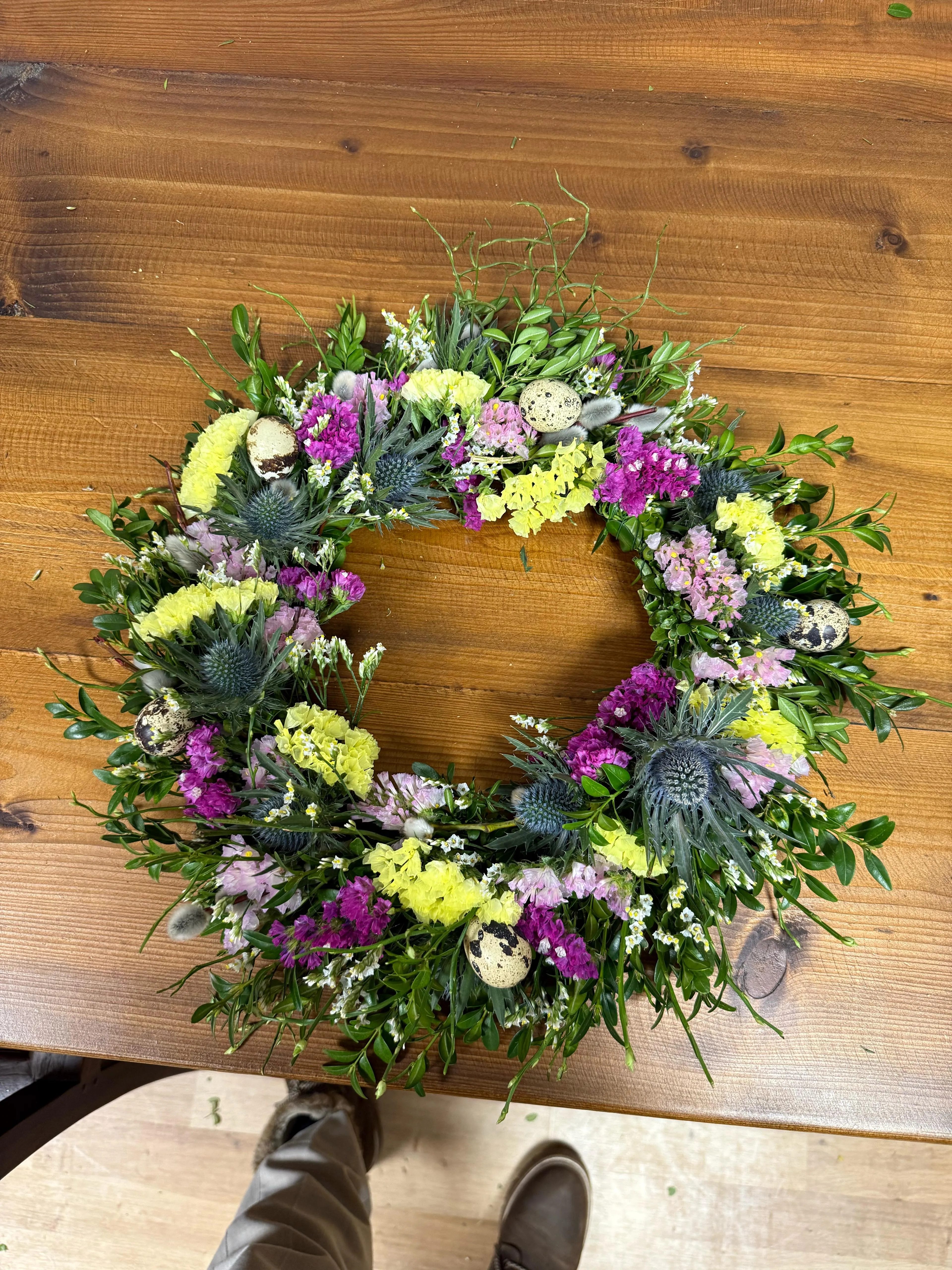 Blumenkranz mit Eiern auf Holztisch.