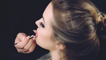 Visagist trägt Lippenstift auf Frau drinnen auf.