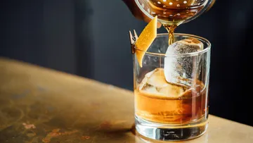 Cocktail being poured into glass on table.