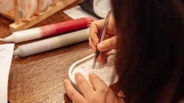 Person crafting candles with tweezers on table.