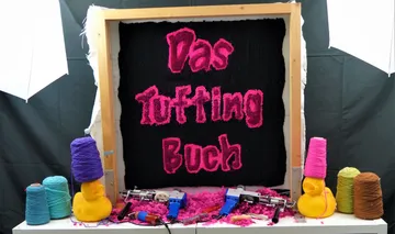 Tufting-Rahmen zeigt deutschen Text, umgeben von Garn.
