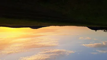 Sunset over grassy landscape with hills.