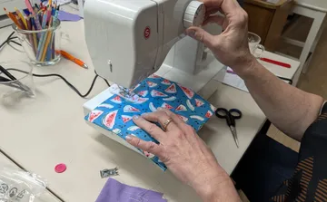 Hands using sewing machine with watermelon fabric.