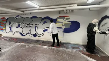 Zwei Personen sprayen Graffiti im Keller.