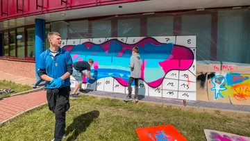 Menschen malen buntes Wandbild auf nummerierter Wand.
