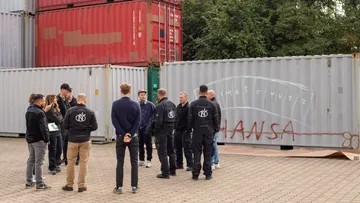 Men standing near stacked shipping containers outdoors.