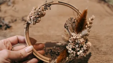 Hand hält Blumen-Hoop auf Holztisch.