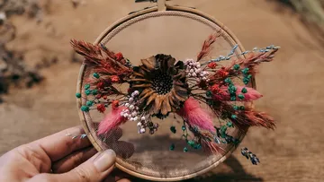 Hand hält bestickten Reifen mit Trockenblumen.
