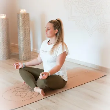 Frau meditiert drinnen auf Yogamatte.