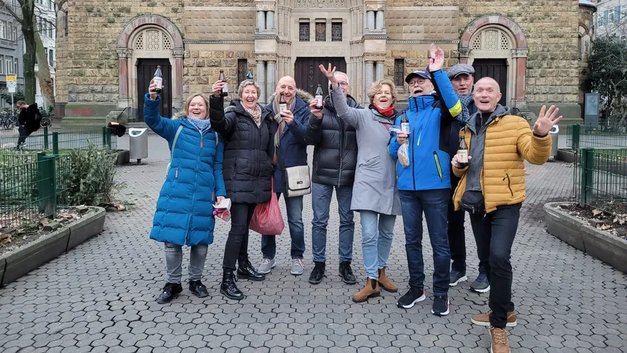 Gruppe von Menschen jubelt mit Getränken vor Gebäude.